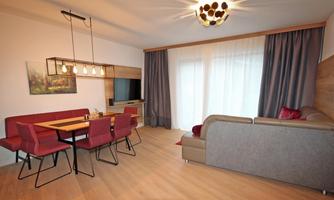 A modern living room with a comfortable sofa and a dining table for four people. Large windows provide plenty of daylight.
