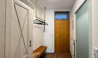 A modern hallway with a wooden shelf and a coat rack. The wall is bright and there is a wooden entrance door.