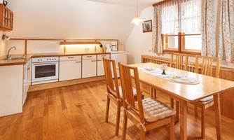 A bright and inviting kitchen with modern appliances and a large dining table. Wooden flooring and windows create a friendly atmosphere.