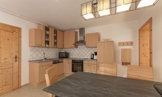 A modern kitchen with light wood cabinets and a large dining table. The amenities include a stove, a microwave, and beautiful lighting.