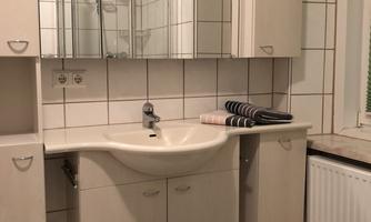 A modern bathroom with a sink and a large mirror. Towels are neatly stacked on the shelf.