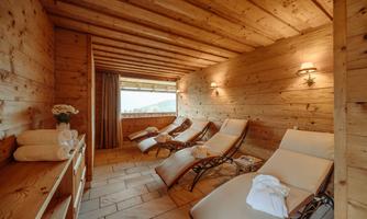 A relaxing room with wooden paneling and loungers. Through the window, one looks out at a picturesque view.