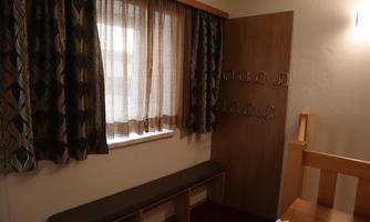 A simple room with a window, curtains, and a bench. On the wall hangs a wooden cabinet with hooks.