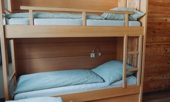 A bright, modern room with a wooden bunk bed. The beds are equipped with light blue bed sheets and pillows.