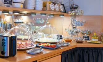 An inviting breakfast buffet in a bright kitchen. There are various dishes under glass domes, fresh fruit, and drinks.