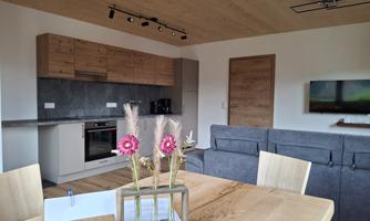 A modernly furnished kitchen with wooden cabinets and a cozy living area. There are flowers on the table and an informational sign.