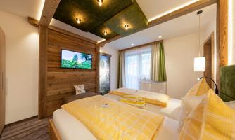 A cozy bedroom with two beds and yellow bedspreads. A television and windows with a view outside complement the modern decor.