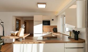 A modern kitchen with light furniture and wooden surfaces. Daylight streams through the windows, creating an inviting atmosphere.