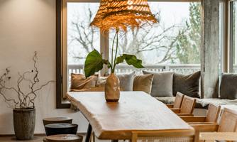 A stylish dining area with a large wooden table and comfortable chairs. A modern lamp and a plant give the room an inviting atmosphere.