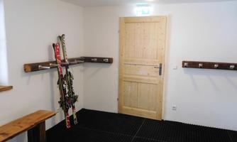 A ski storage room with a wooden bench and hooks on the wall. Several skis are leaning against the wall.