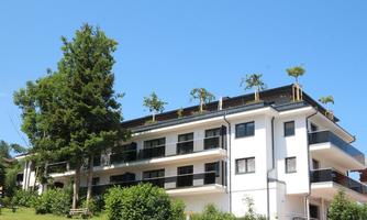 A modern residential building with balconies, surrounded by green landscape. Small trees grow on the roof, adding a special touch.