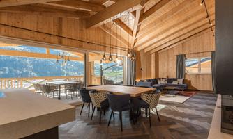 A modern, bright living room with a wooden ceiling and large windows. The room is tastefully furnished and offers a view of the mountains.