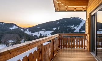 A wooden balcony overlooking snow-capped mountains at dusk. The landscape is calm and wintry.