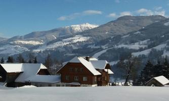 A picturesque winter landscape with snow-covered hills and mountains in the background. In the foreground stand traditional wooden and half-timbered houses.
