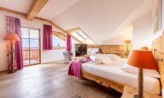 A cozy bedroom with wooden details and large windows. The room is bright and friendly, featuring a large bed and modern lamps.
