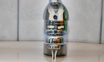 A shiny stainless steel faucet that lets water flow into a sink. The surroundings are bright and modern.