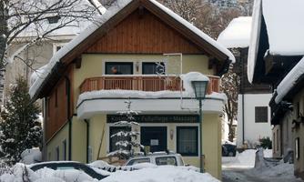 A cozy house in the snow with a wooden balcony. Surrounded by snow-covered trees and other buildings.
