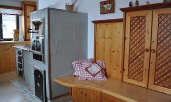 A cozy kitchen with an old stove and wooden furniture. On a bench, there are cushions in a checked pattern.