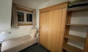 A simple room with a cozy bed and a wooden wardrobe. The room has a window and a small bedside lamp.