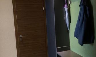 A hallway with a wooden door and a coat rack. There is a wall shelf and a modern shoe cabinet.