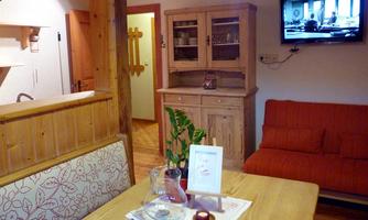A cozy living space with wooden details, a red sofa, and a TV on the wall. A table with decoration and a plant is also visible.