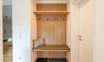 A cozy entrance area with wooden shelves and a seating area. Several hooks for jackets and bags are hanging on the wall.