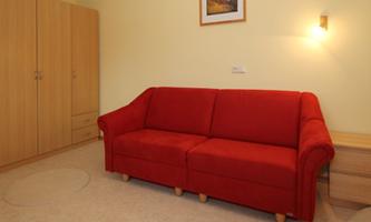 A red sofa is in a bright room. There is a cabinet and a picture on the wall.