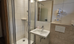 A modern bathroom with a shower, a sink, and a toilet. The walls are light and there is a mirror above the sink.