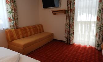A simple, cozy hotel room with a comfortable sofa and a television. Large windows ensure plenty of daylight.