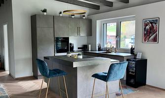A modern kitchen with an island and chairs in light blue. Large windows provide plenty of natural light and a welcoming atmosphere.