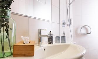 A modern bathroom with an elegant sink and a mirror. There is a clear faucet, a soap dispenser, and a decorative vase with plants.