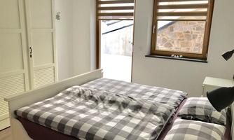 A cozy bedroom with a large bed and checked bedspreads. There are two windows that let in plenty of light and provide a natural view outside.