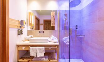 The image shows a modern bathroom with a glass shower and an elegant sink. Beige tiles and wooden details create a cozy atmosphere.