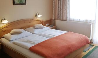 A cozy bedroom with a large bed and an orange throw. The large window front lets in a lot of daylight and creates a bright atmosphere.