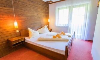 A bright, cozy bedroom with wooden paneling and two beds. The room has large windows that let in a lot of light.