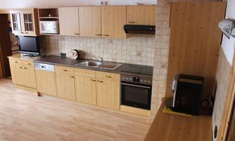 A modern kitchen with wooden cabinets and various appliances. The floor is made of light wood, and the room is well-lit.