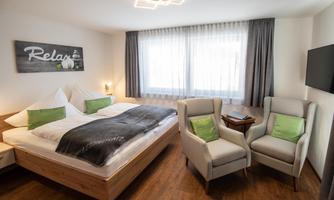 A bright and modern room with a double bed and two cozy armchairs. Large windows provide plenty of daylight and a relaxed atmosphere.