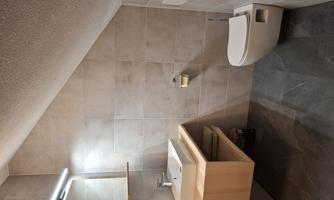 A modern bathroom with tiled walls. There is a sink with a wooden shelf and a toilet.