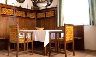A cozy dining area with wood-paneled walls and a table in the center. The chairs have orange fabric, and there is a rustic-style ceiling light.