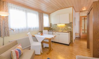 A cozy kitchen with a dining area and a sofa. The windows let in plenty of daylight and the walls are cheerfully designed.