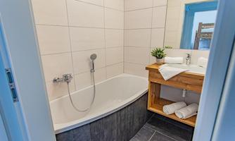 A modern bathroom with a bathtub and a wooden table. Fresh towels and plants create an inviting atmosphere.
