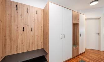 A modern hallway with a wooden coat rack and a white wardrobe. The floor is made of wood, and there is a green carpet.
