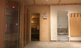 A modern wellness area with a sauna and infrared cabin. The walls are made of wood and the floor is tiled.