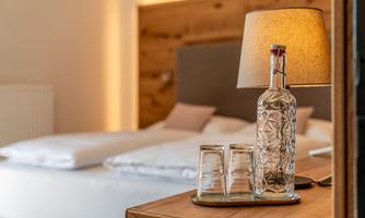 A stylish bedroom with a comfortable bed and warm light. On the bedside table, there is a water carafe and glasses.