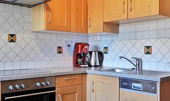 A modern kitchen with wooden cabinets and stainless steel appliances. It includes a stove, a kettle, and a sink.
