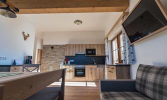 A modern kitchen with wood and stone accents. In the foreground, there is a dining area and a comfortable sofa.