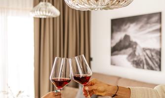 Two people clink wine glasses in a cozy living space. The room is bright and modernly decorated.