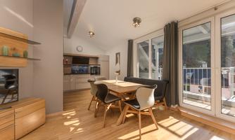 A modern dining room with a wooden table and comfortable chairs. Large windows provide plenty of daylight and a view outside.