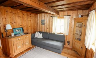 A cozy living room with wood paneling and a gray sofa. Next to the sofa is a wooden cabinet and a table with a lamp.
