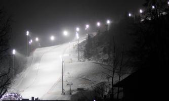 A illuminated ski slope at night. The snow is fresh and the surroundings appear calm and winter-proof.